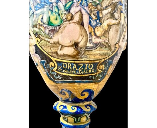 Large majolica vase with lateral handles in the shape of winged figures. Decorated with inscription: Horace defeated the Sabines and medallion with a male profile. Manufacture by Berardino Pepi. Siena.     